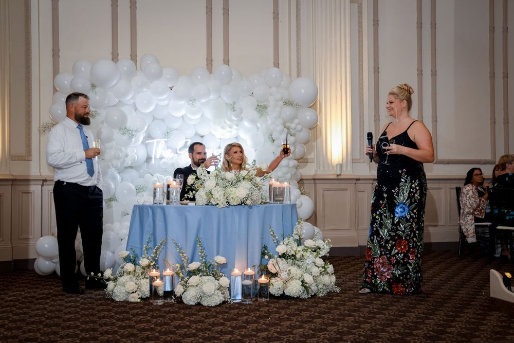 Wedding reception scene with decorative white flower wall and head table setup.