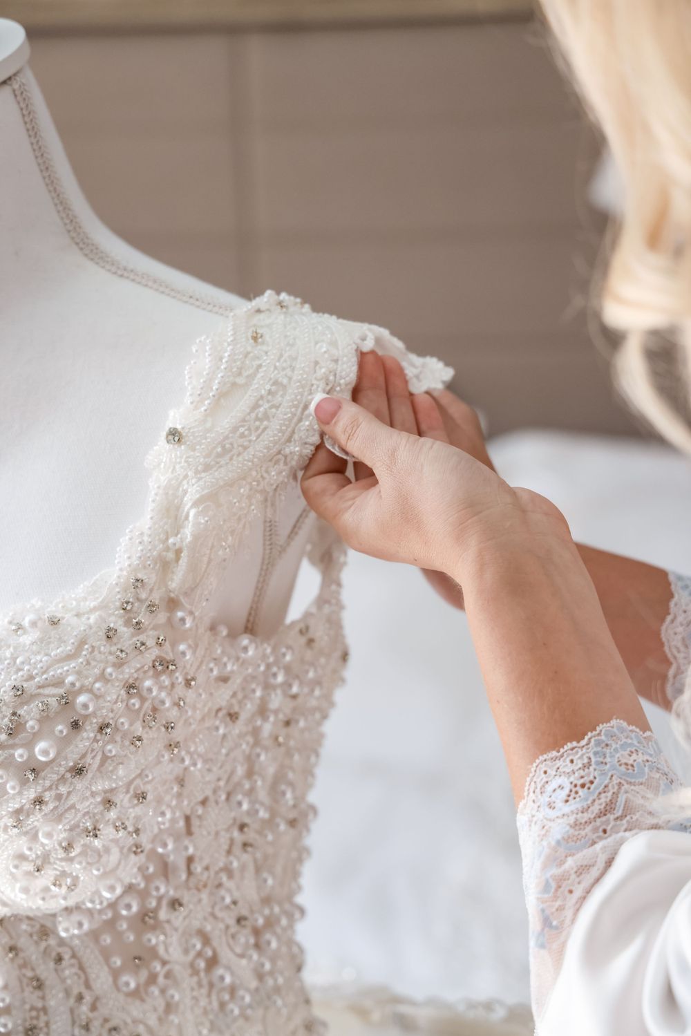 Close-up of hands adjusting delicate beadwork and lace details on a white wedding dress.