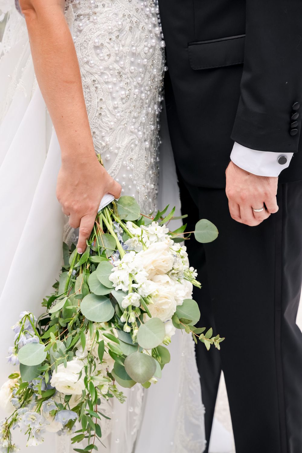 Close-up of wedding couple holding white and green bouquet with eucalyptus leaves.