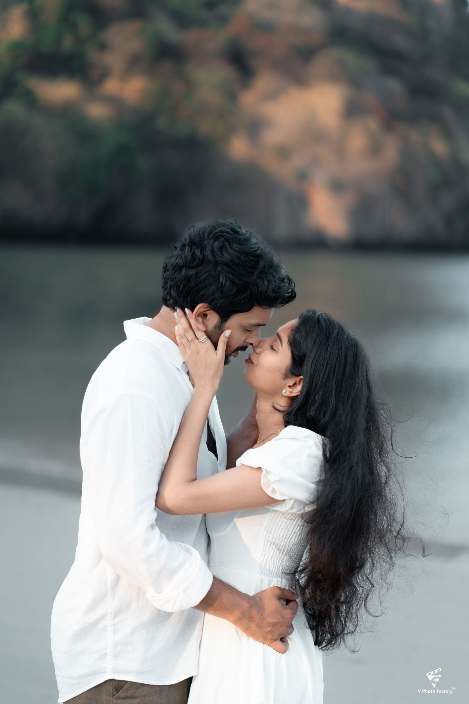 Romantic couple embracing by lakeside in white outfits during golden hour photoshoot.