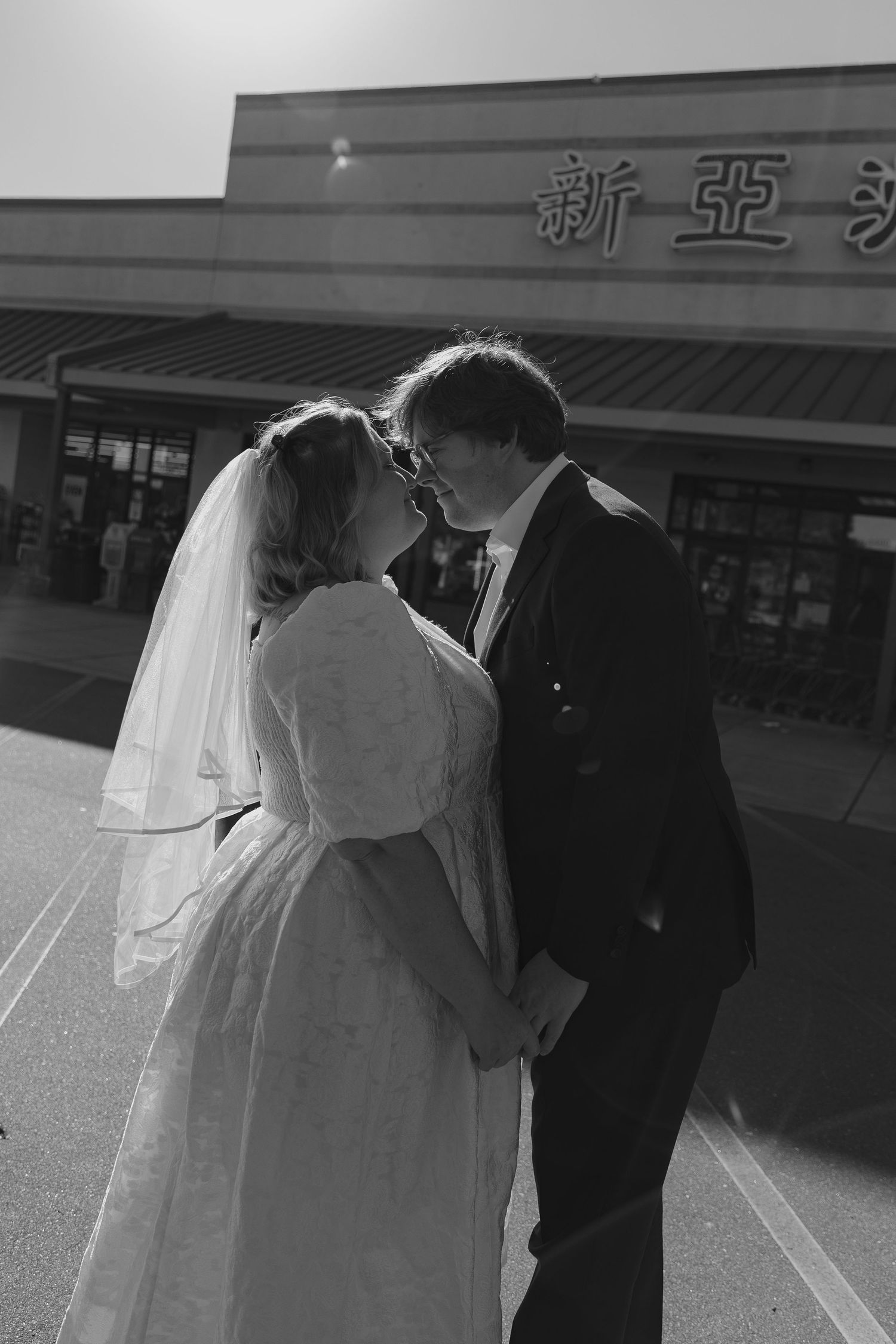 A romantic black and white portrait of a couple in wedding attire outside a storefront.