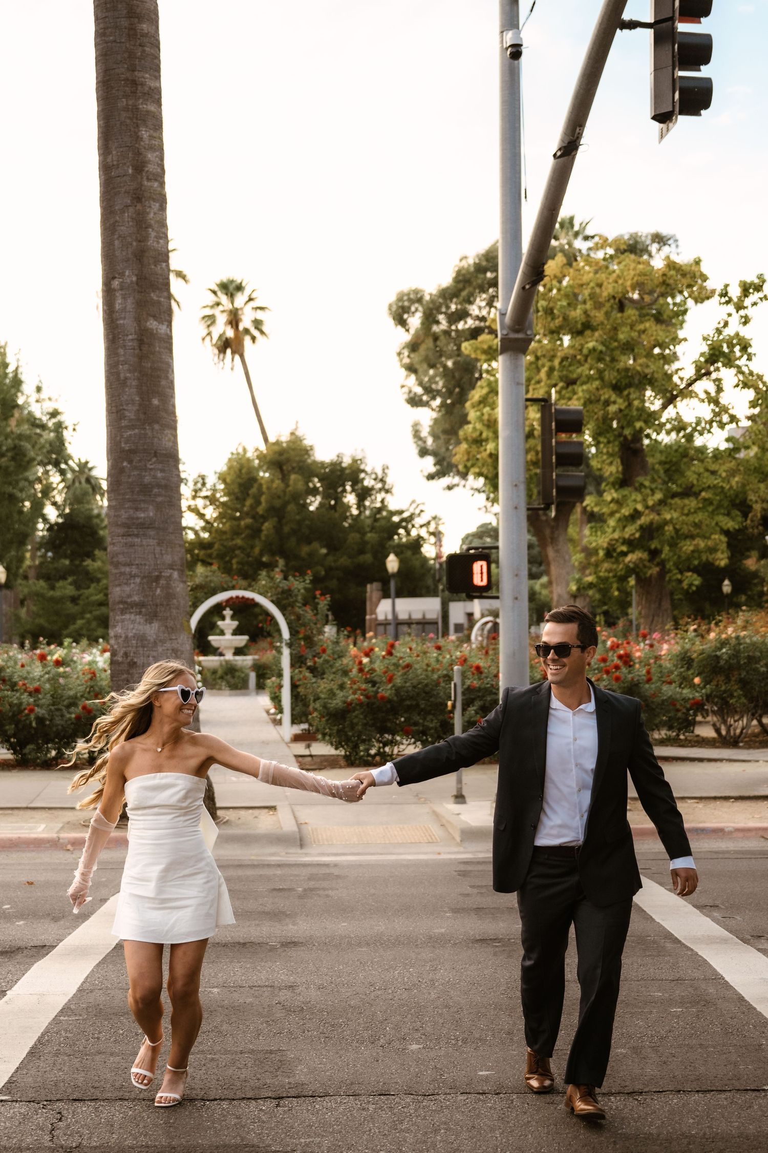 A playful couple dancing and twirling on a palm tree-lined street at sunset.