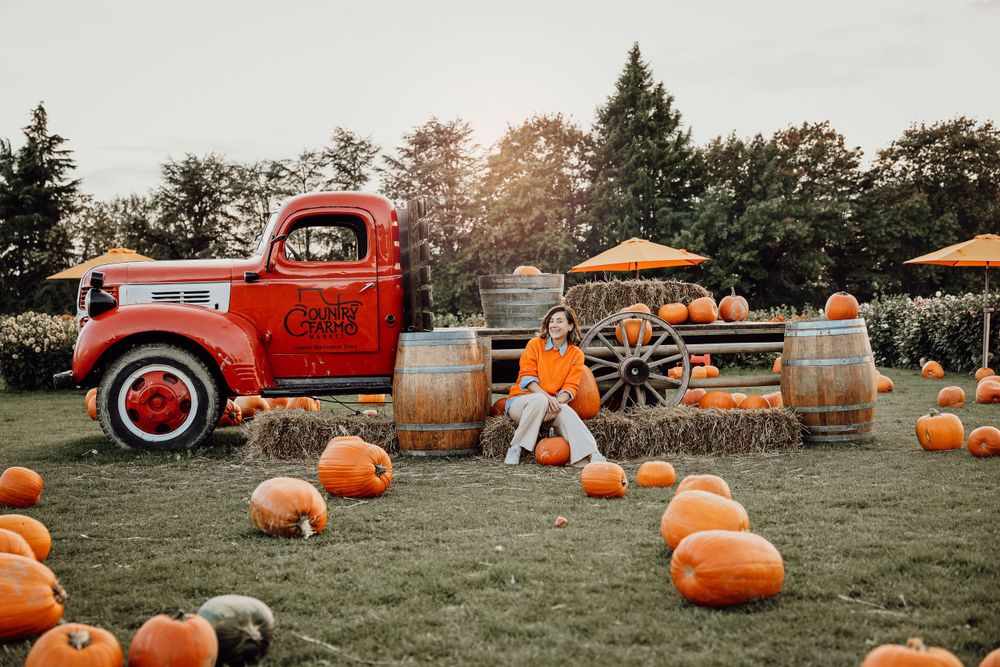 Vintage red pickup truck with pumpkins and wooden barrels in an autumn farm setting.