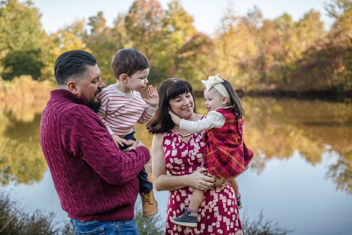 Family gathering by a serene pond in autumn wearing cozy sweaters.