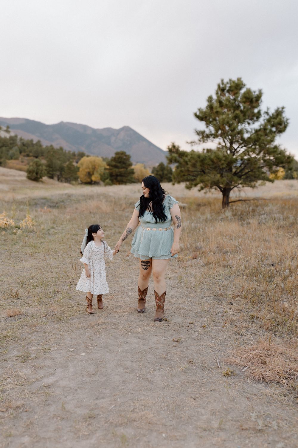 Holding hands while walking along a mountain trail in coordinated dresses and boots. Colorado Springs Photographer.