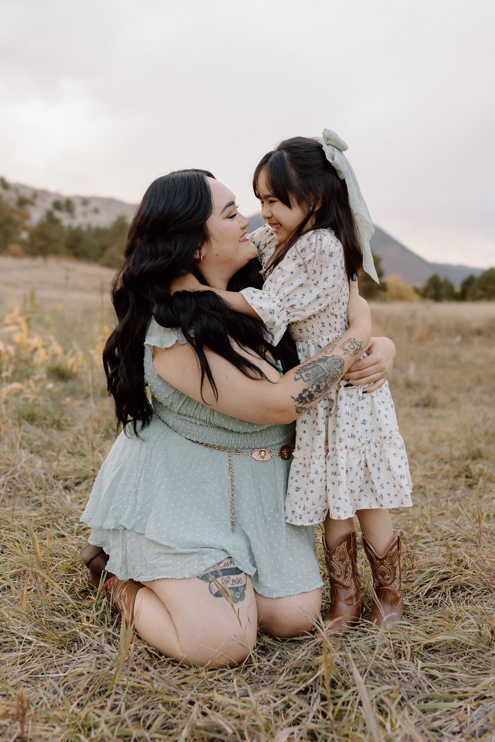Sweet moment between parent and child wearing floral dress and cowboy boots in a field. Colorado Springs Photographer.