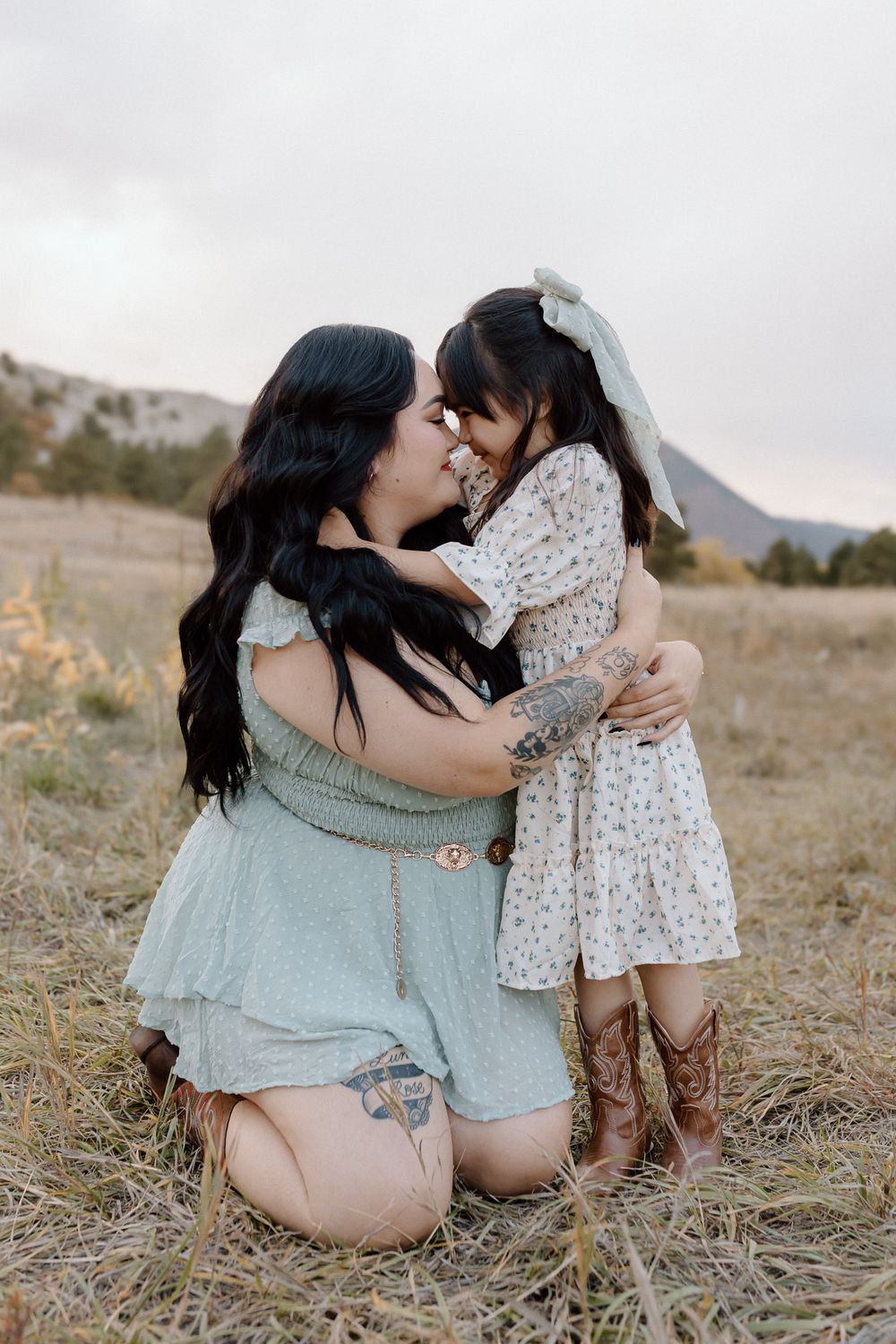 Tender embrace shared while kneeling in a mountain field wearing complementary outfits. Colorado Springs Photographer.