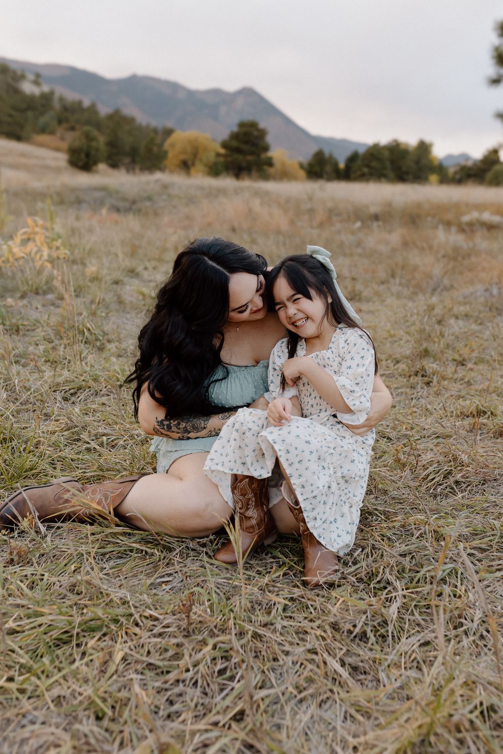 Sharing laughter while sitting together in mountain field wearing coordinated outfits. Colorado Springs Photographer.