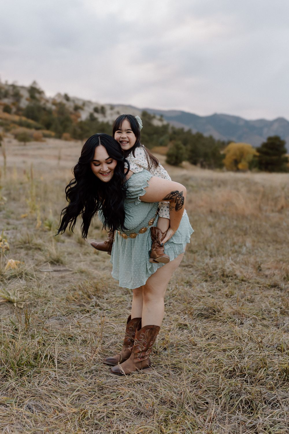 Playful piggyback ride moment captured against a mountainous backdrop on a cloudy day. Colorado Springs Photographer.