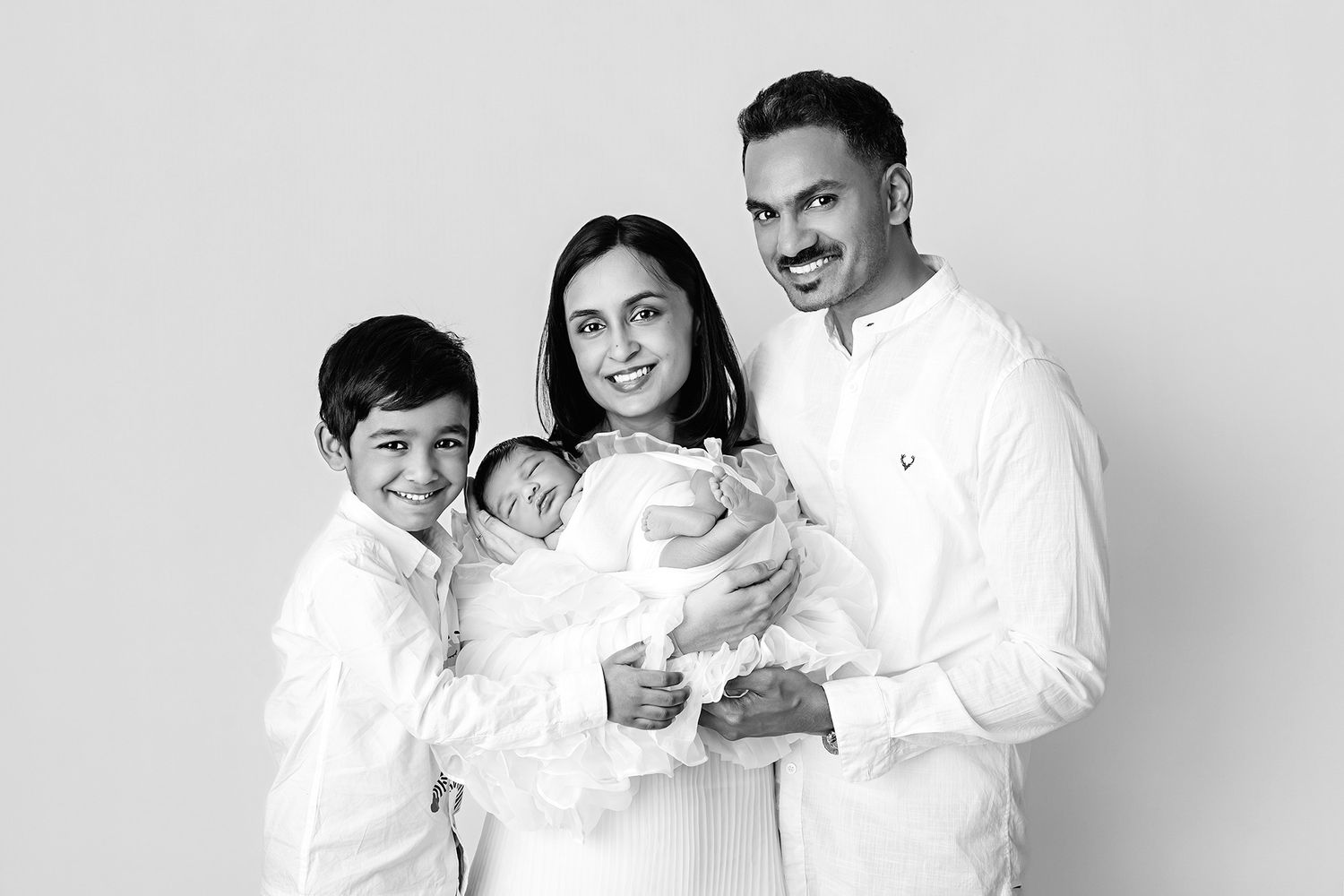 Family portrait in white outfits against neutral background.