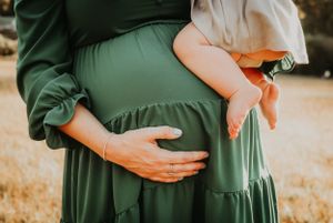 Close-up of hands cradling pregnant belly in green dress.