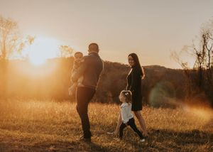 A family walks together through a sunlit field during golden hour.