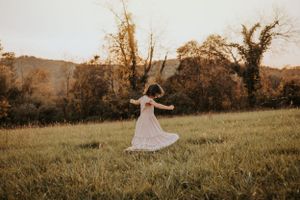A figure in a flowing dress twirls in a sunlit meadow during golden hour.