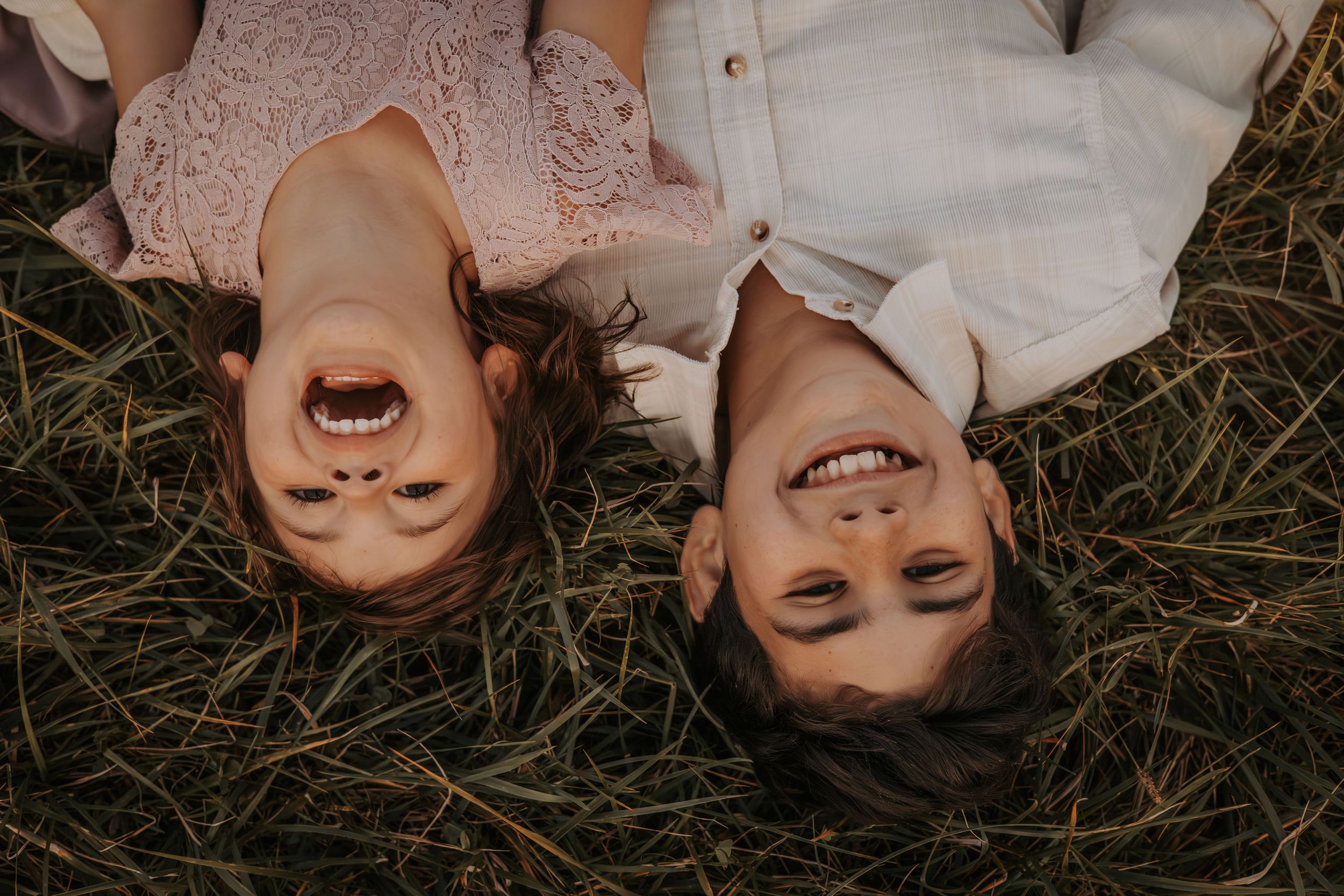 Two people lying in grass sharing joyful laughter during an outdoor photo session.