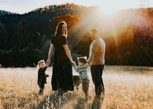 A family stands together in a golden field at sunset with mountains in the background.
