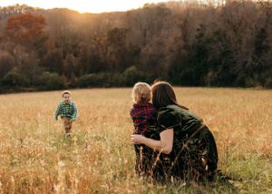 Family watching child run through golden field at sunset.