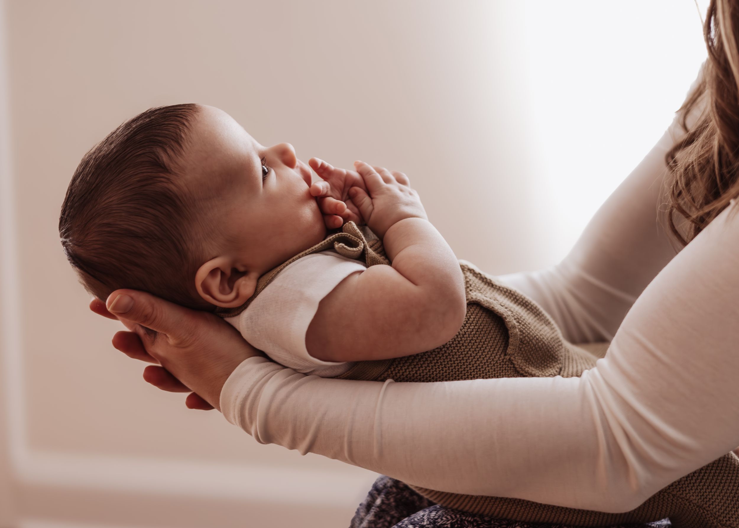 Infant being held up against soft white background in gentle natural light.