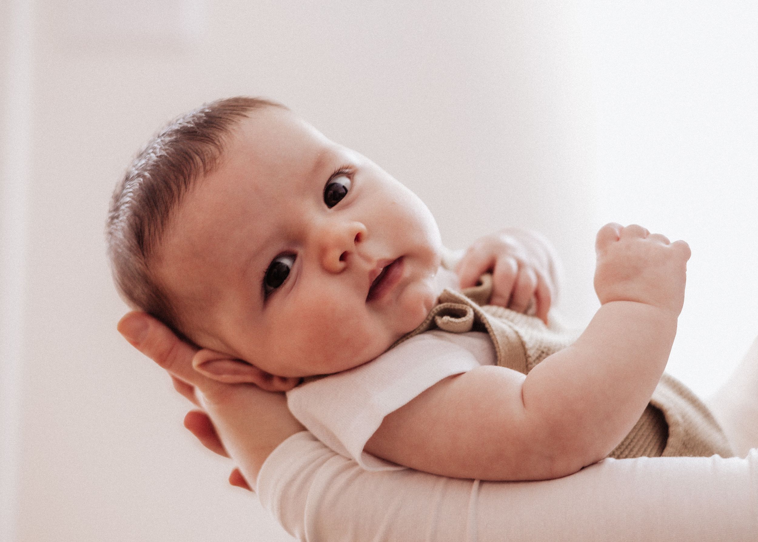Infant in white onesie lying on side against light background.