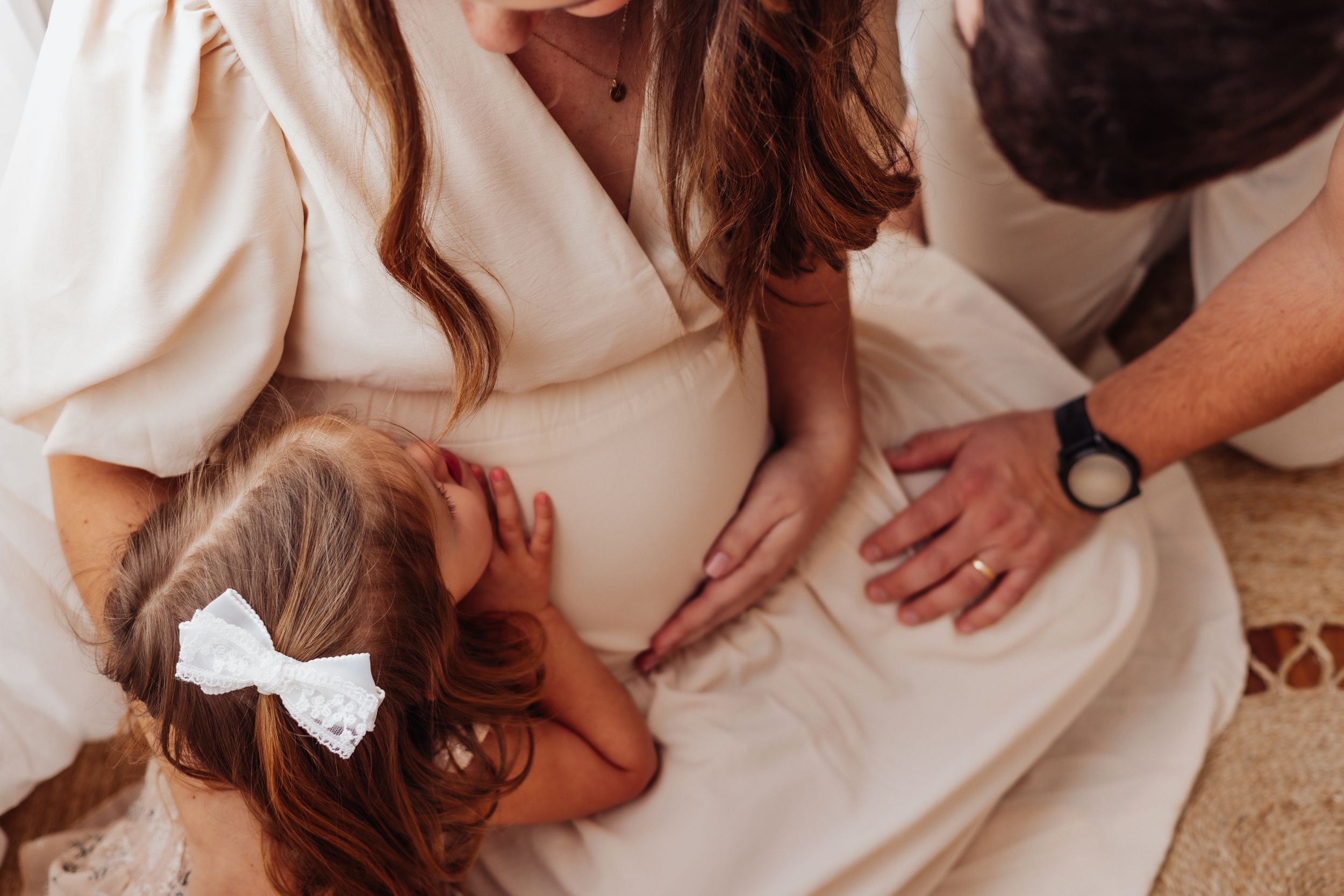 Maternity photo capturing tender family moment in soft neutral tones.