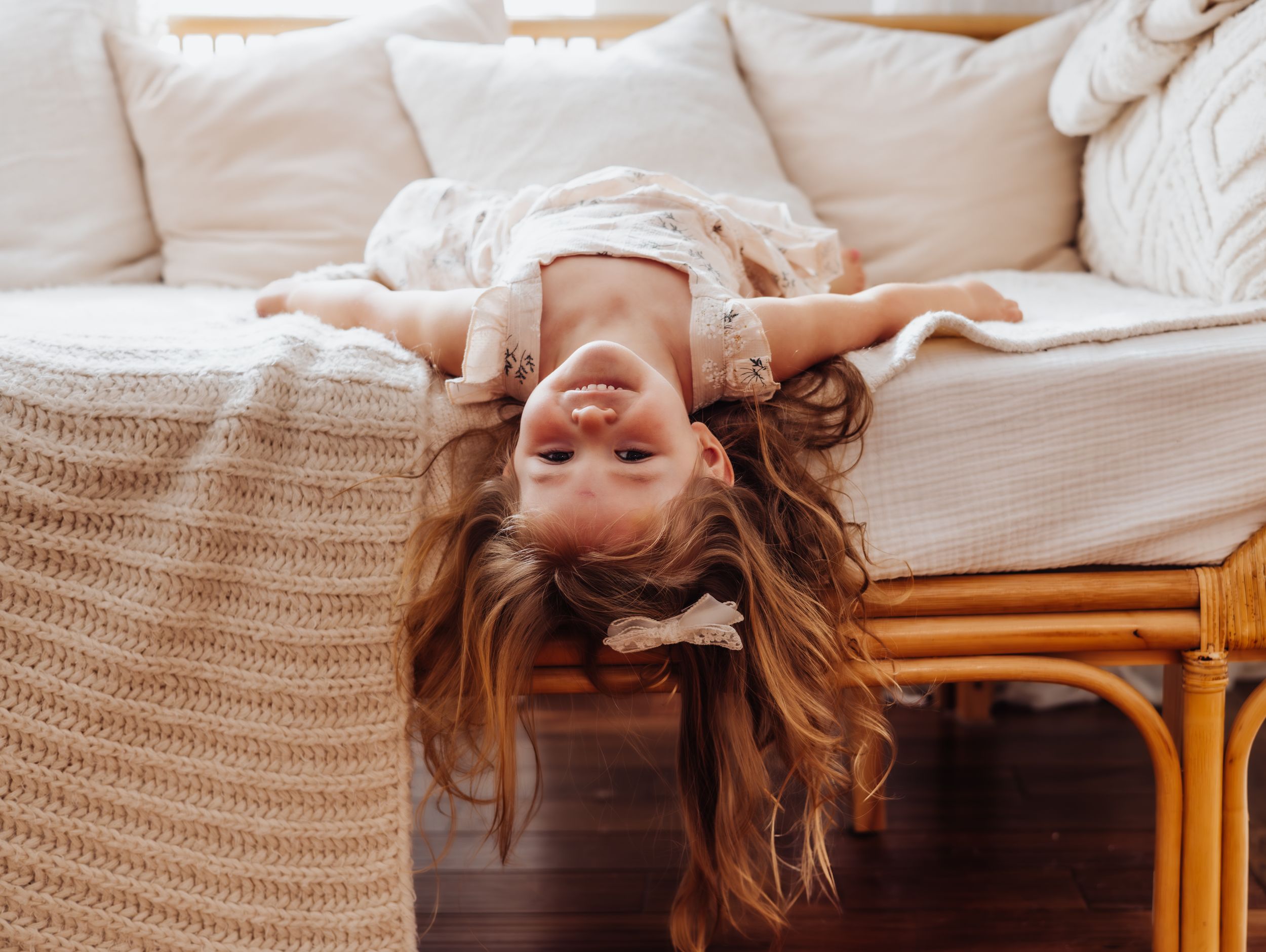 Person in white lying upside down on couch with hair flowing down.