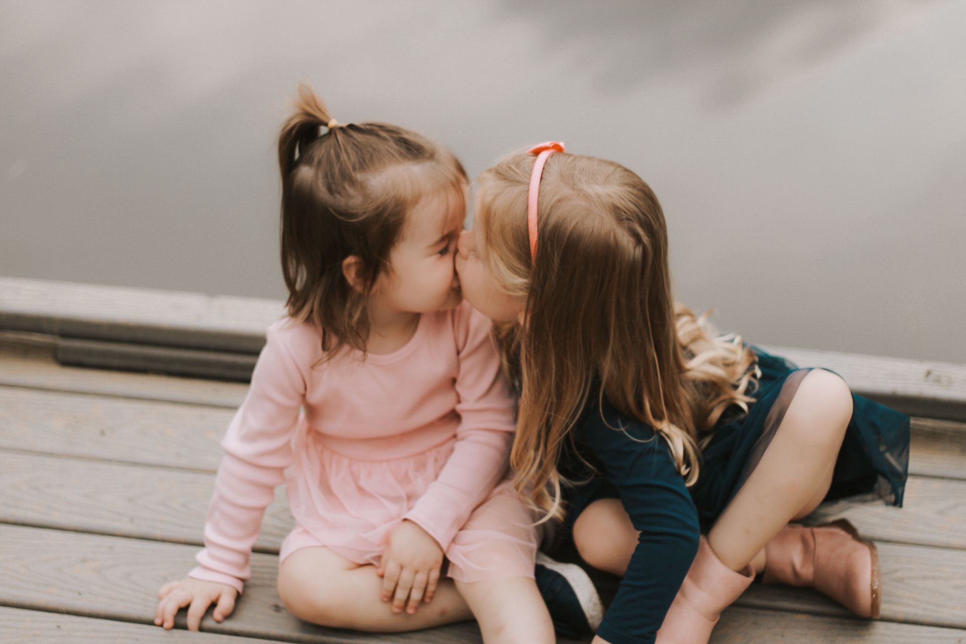 Two young children in pink and blue sitting close together on a grey deck.
