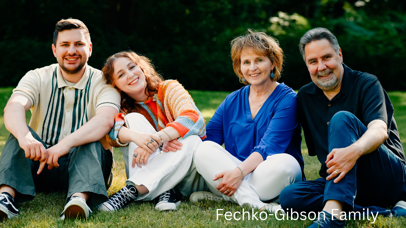 Family of four sitting together on grass during outdoor portrait session.
