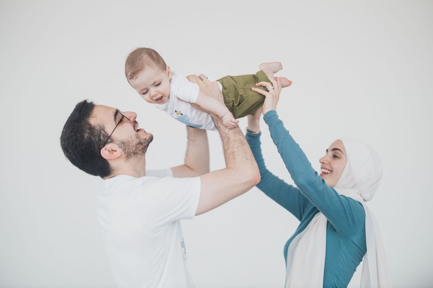A playful family moment with lifted baby against white background.