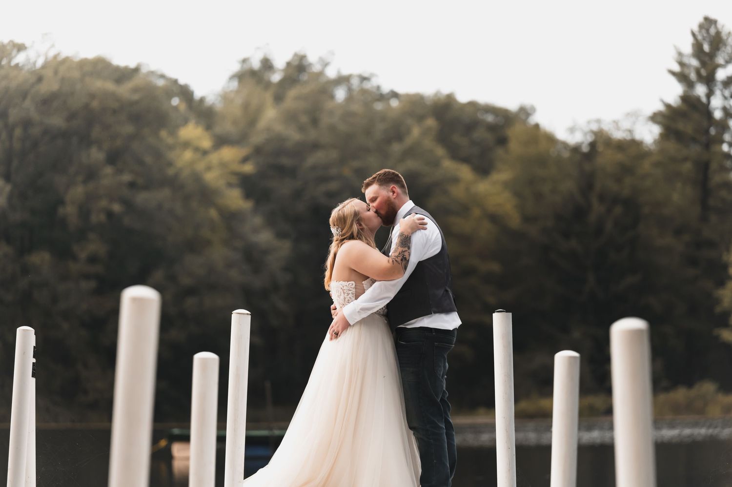 Romantic wedding couple embracing on a dock with white pillars at sunset.