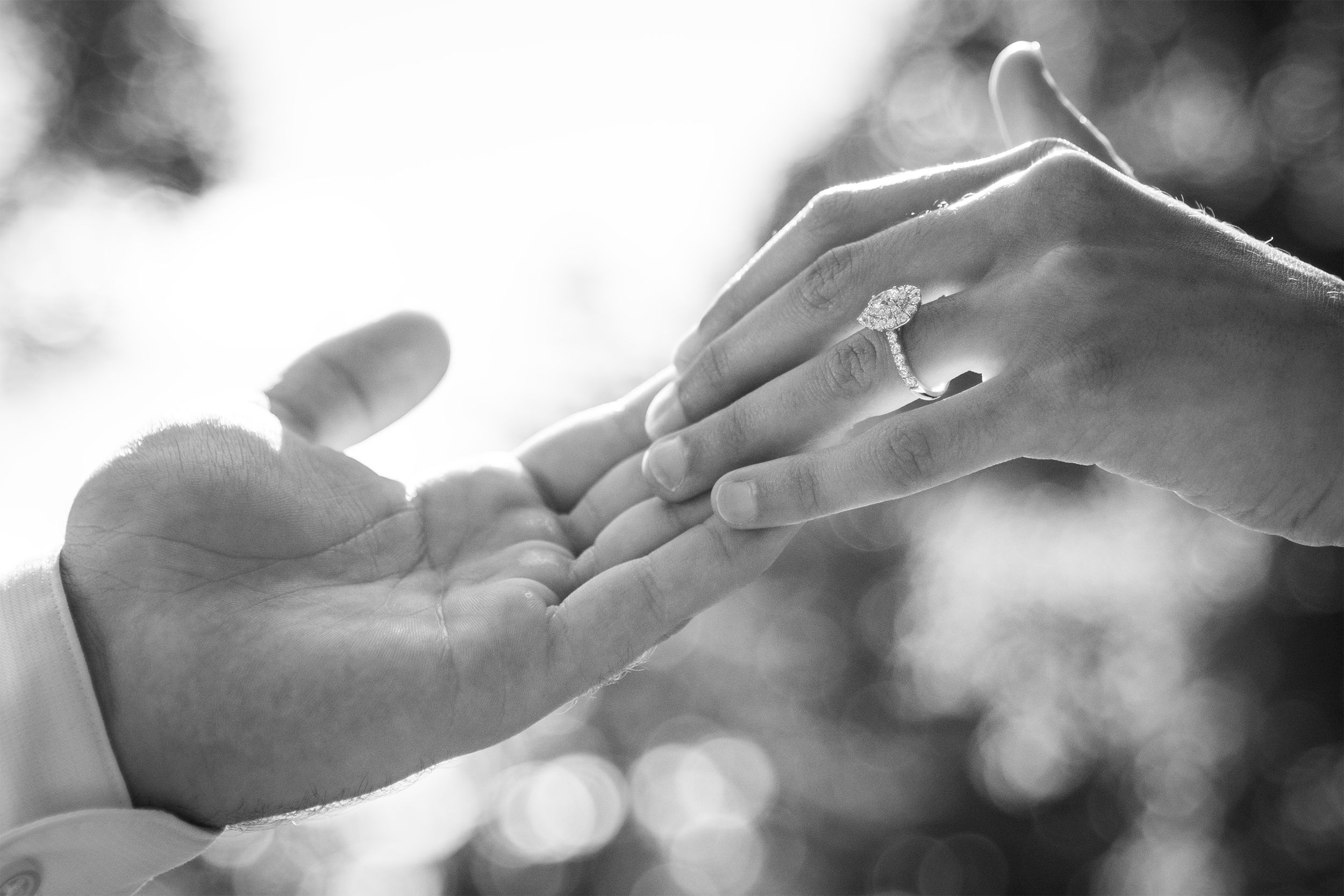 Black and white close-up of hands exchanging a ring during proposal or engagement.