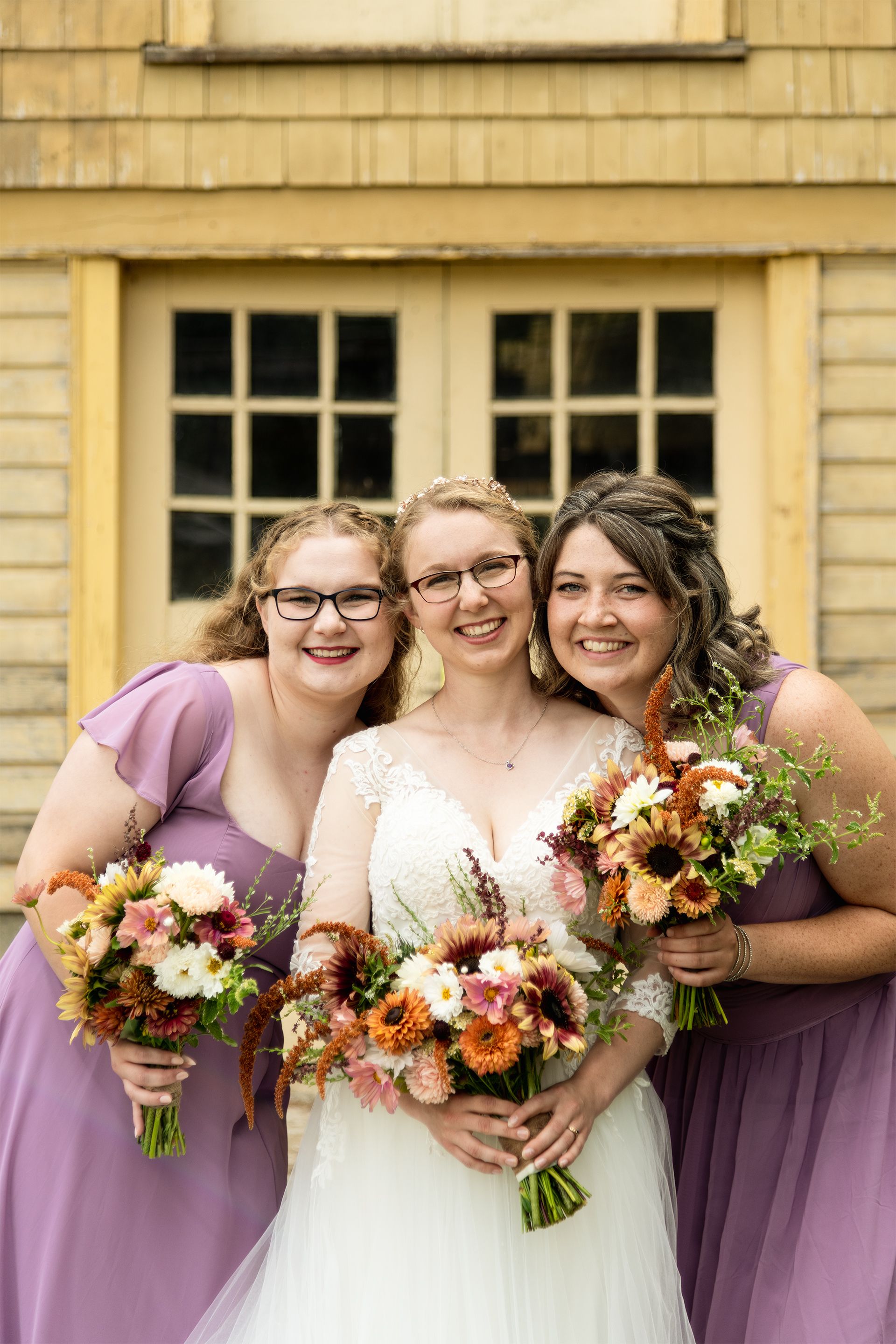 Wedding party with bride and bridesmaids in purple dresses holding autumn-colored bouquets.