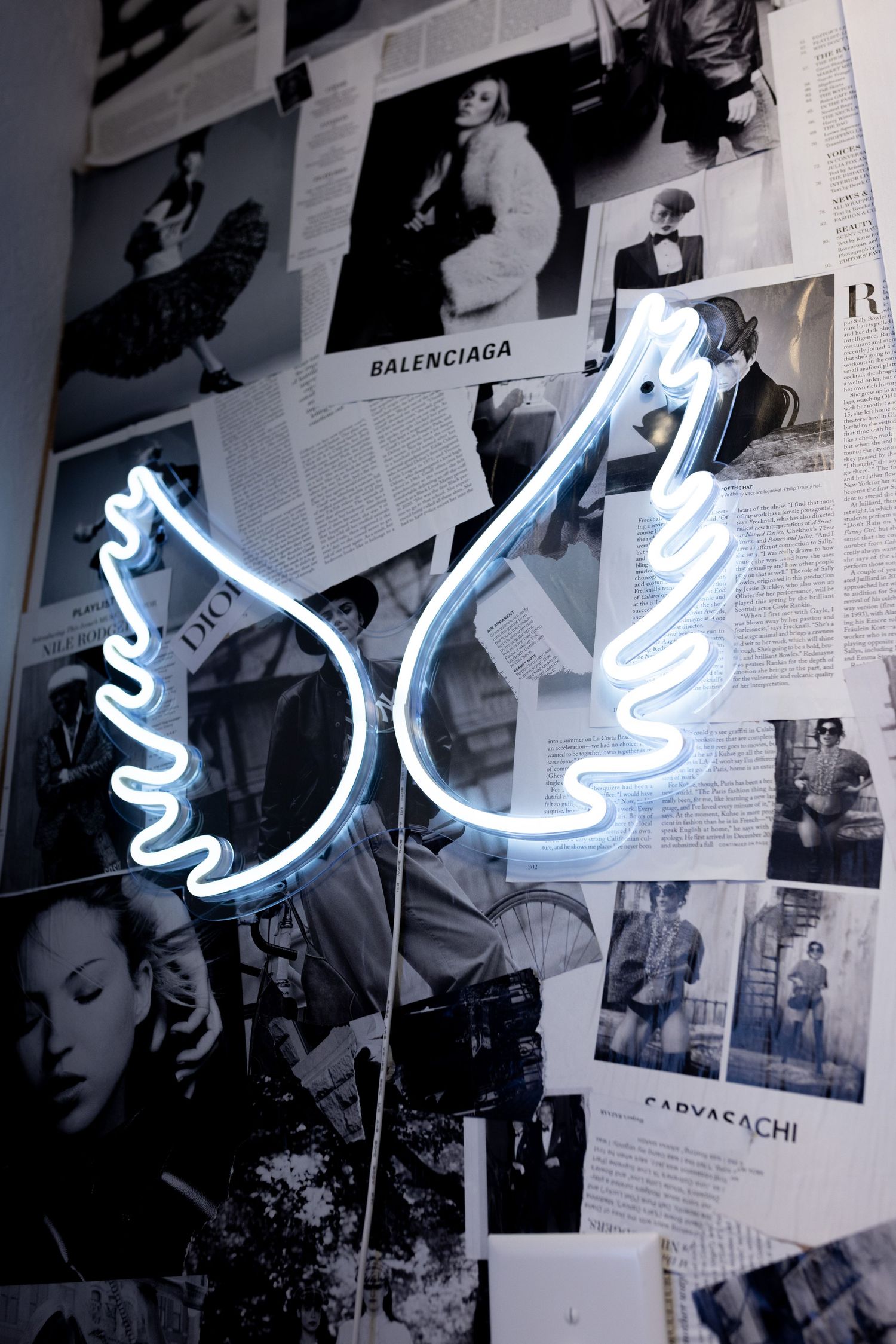 Blue neon light installation mounted on wall covered with black and white fashion photographs.