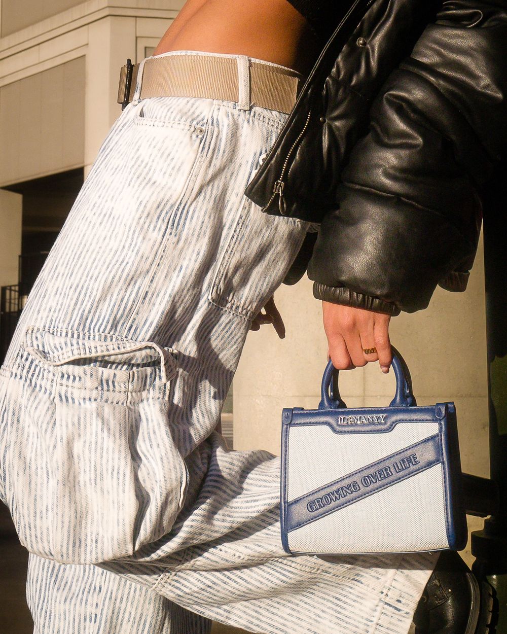 Close-up detail shot of striped cargo pants and small blue designer handbag.