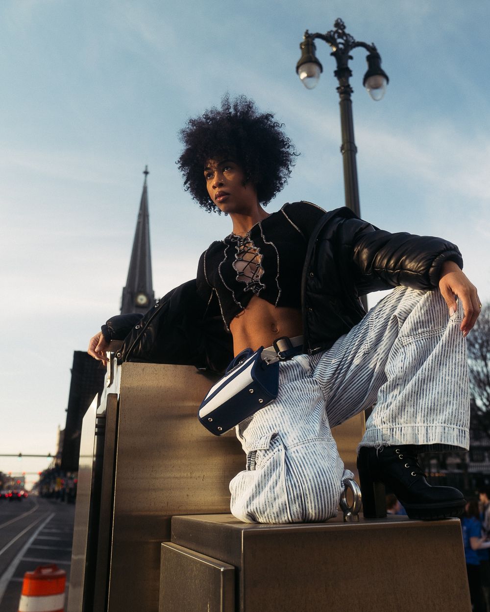 Urban fashion photography with decorative street lamp and church spire in background.