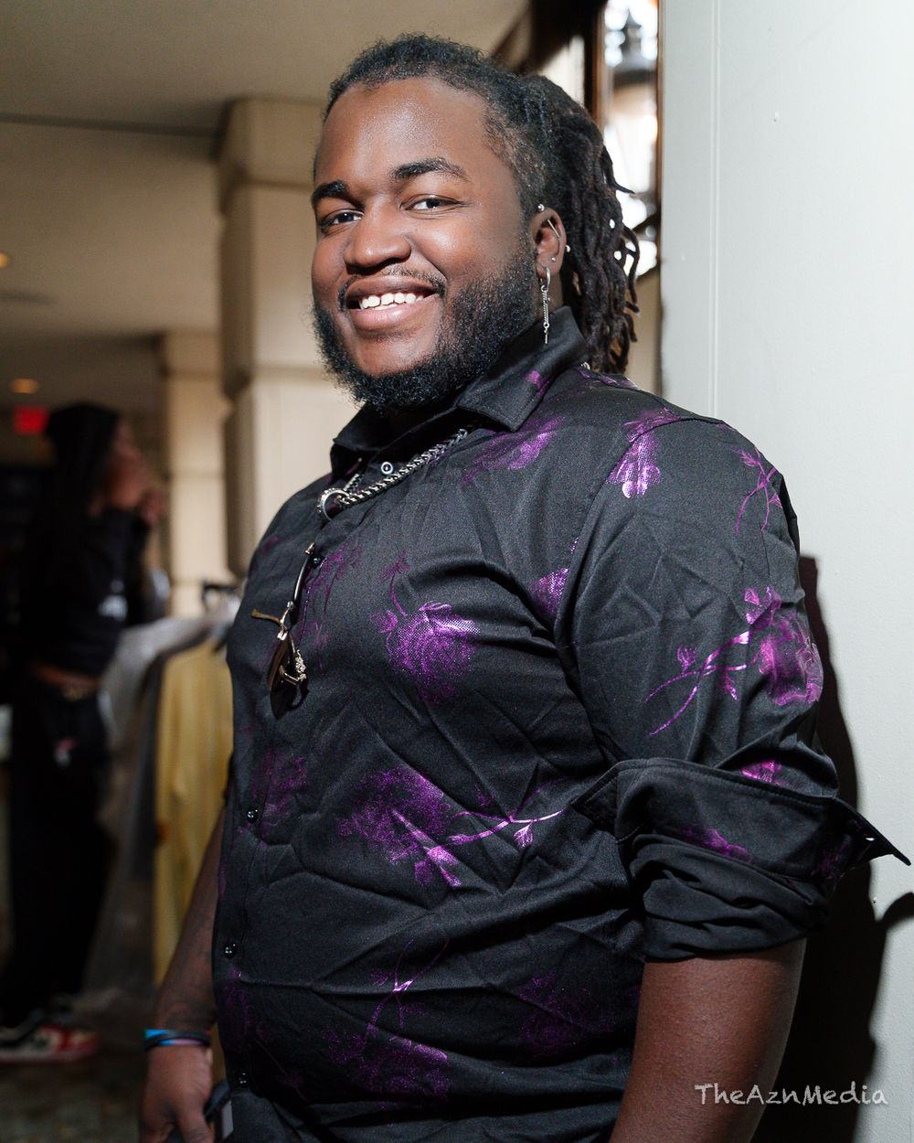 Portrait of person in purple-accented black shirt smiling warmly at camera.