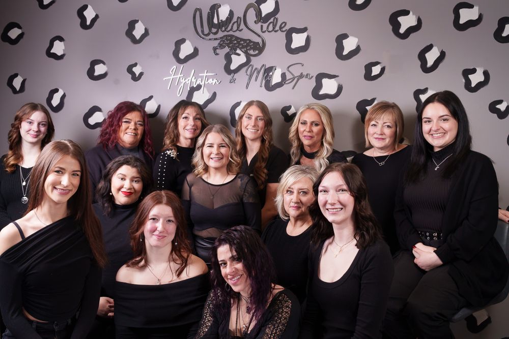 Group photo of salon team members wearing coordinated black outfits against patterned backdrop.