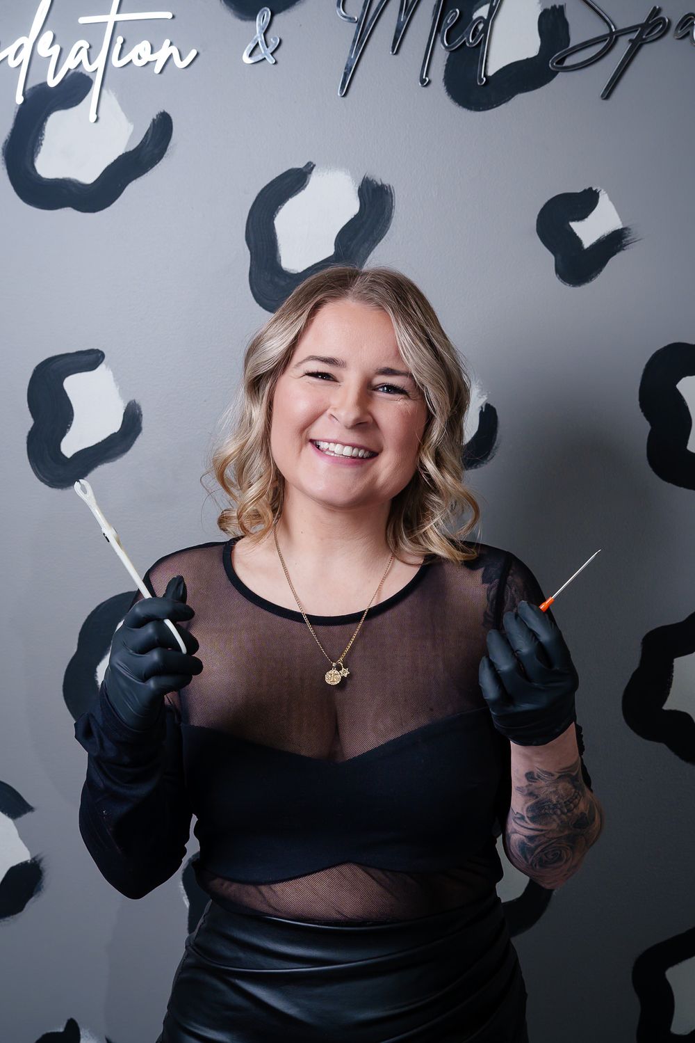 Stylist in black mesh top poses against leopard print wall with styling tools.