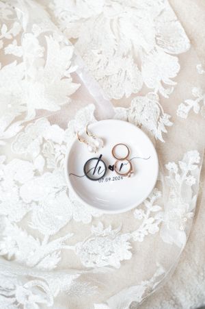 Detail shot of rings in a dish with the wedding date on them on top of the train of the brides wedding dress