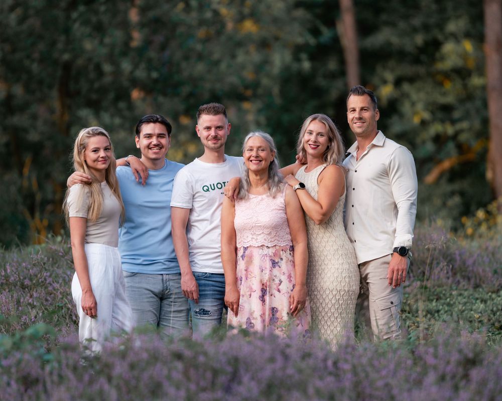 Family group photo session in coordinated outfits among blooming purple flowers.
