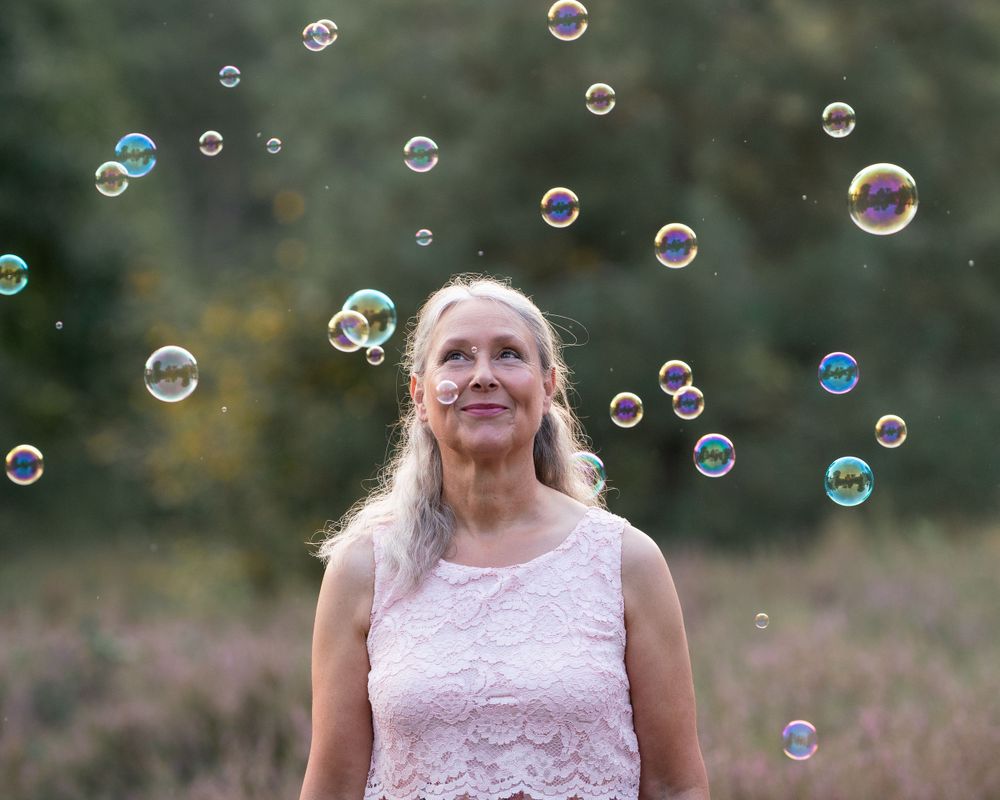 Person in pink dress surrounded by floating soap bubbles in golden evening light.