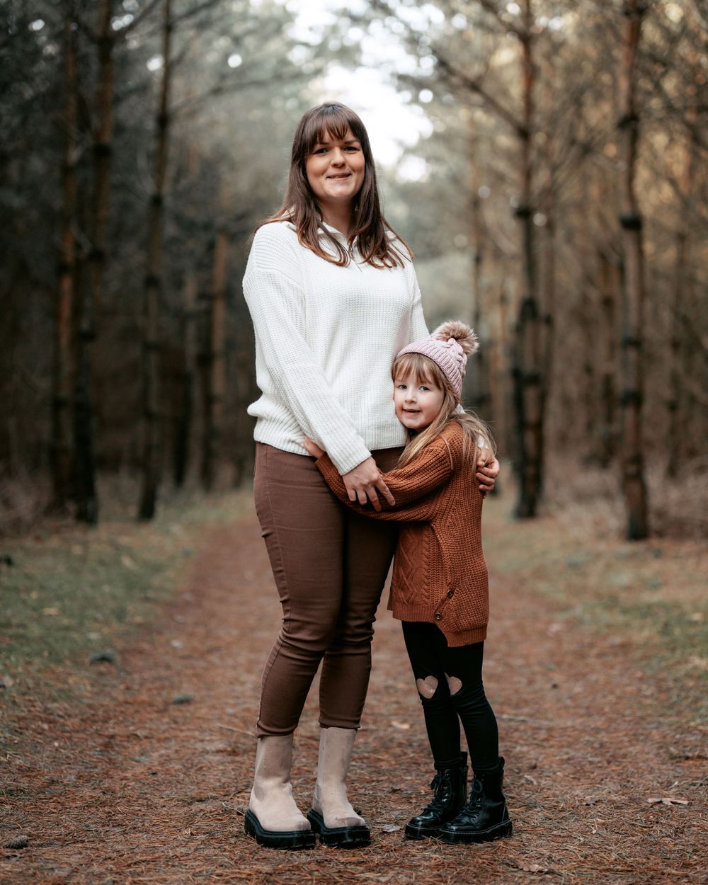 Mother and child share candid moments together on a forested path wearing coordinated brown and white outfits.