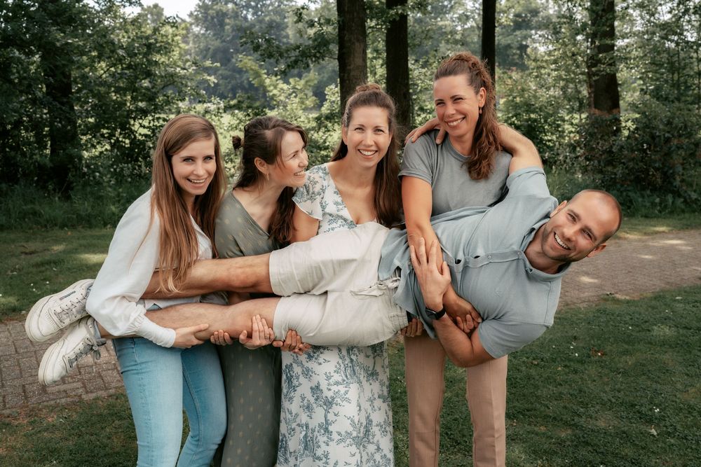 Playful family photo session with multiple people embracing and laughing together outdoors.
