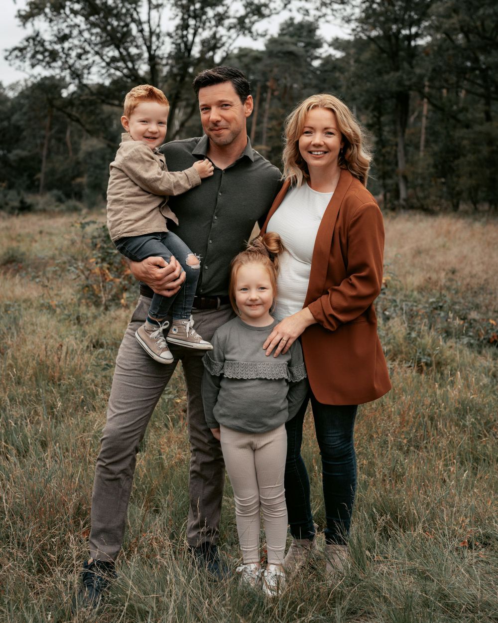 A family of four poses together outdoors in casual fall attire.