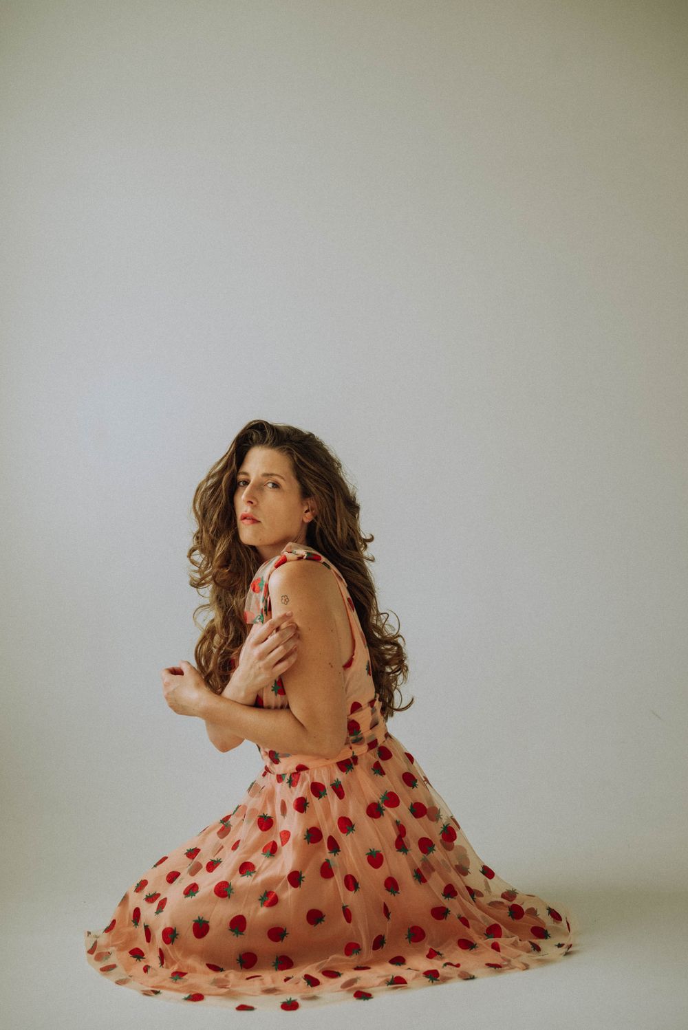 Figure in polka dot dress poses gracefully against plain wall in natural light.