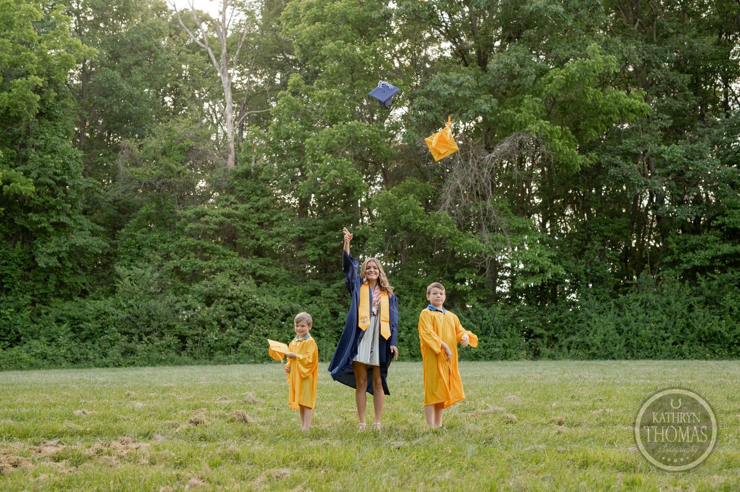 Graduation caps fly through air as graduates celebrate in yellow gowns.