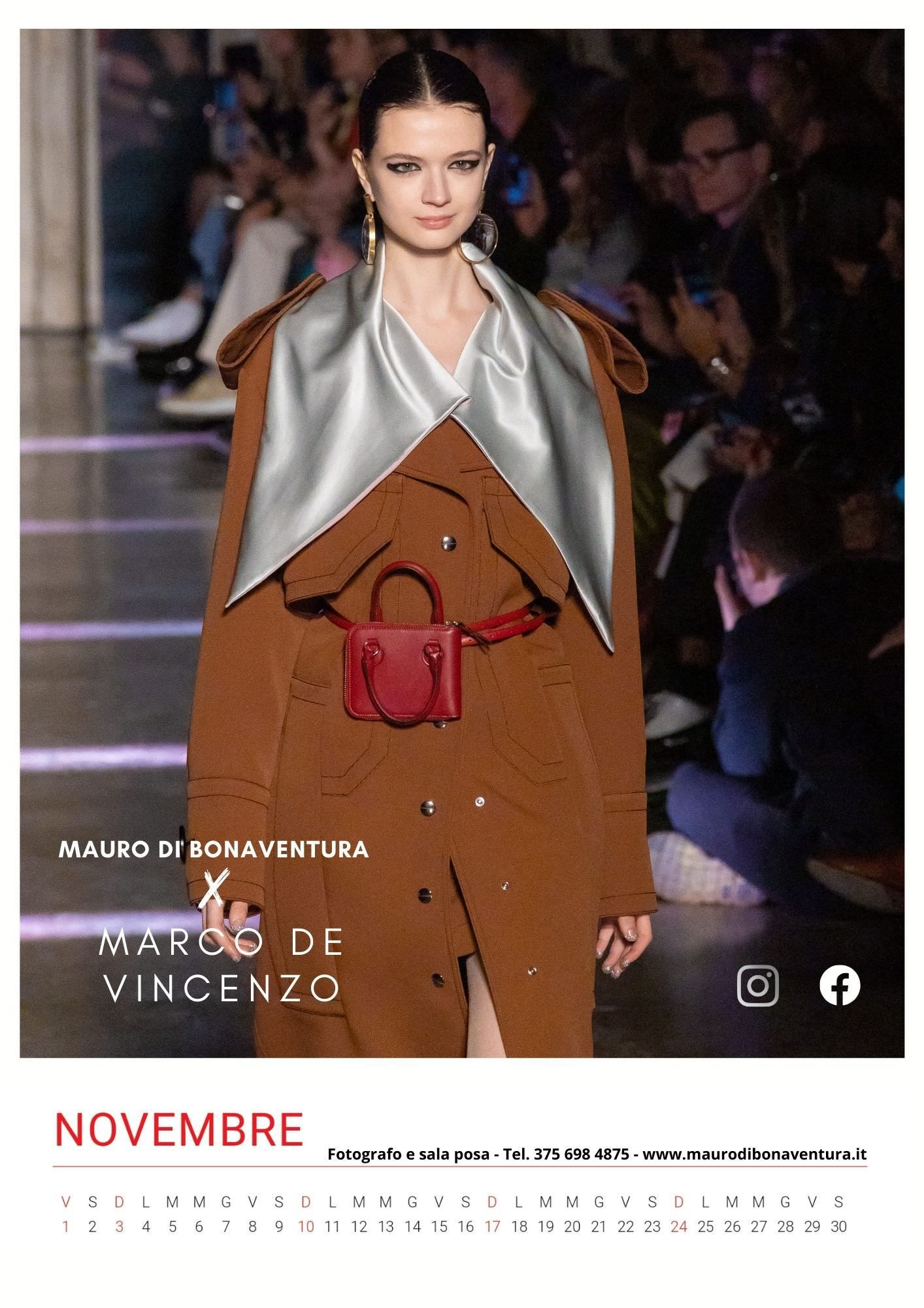 Fashion model wearing brown coat with silver lapels on runway during fashion show.