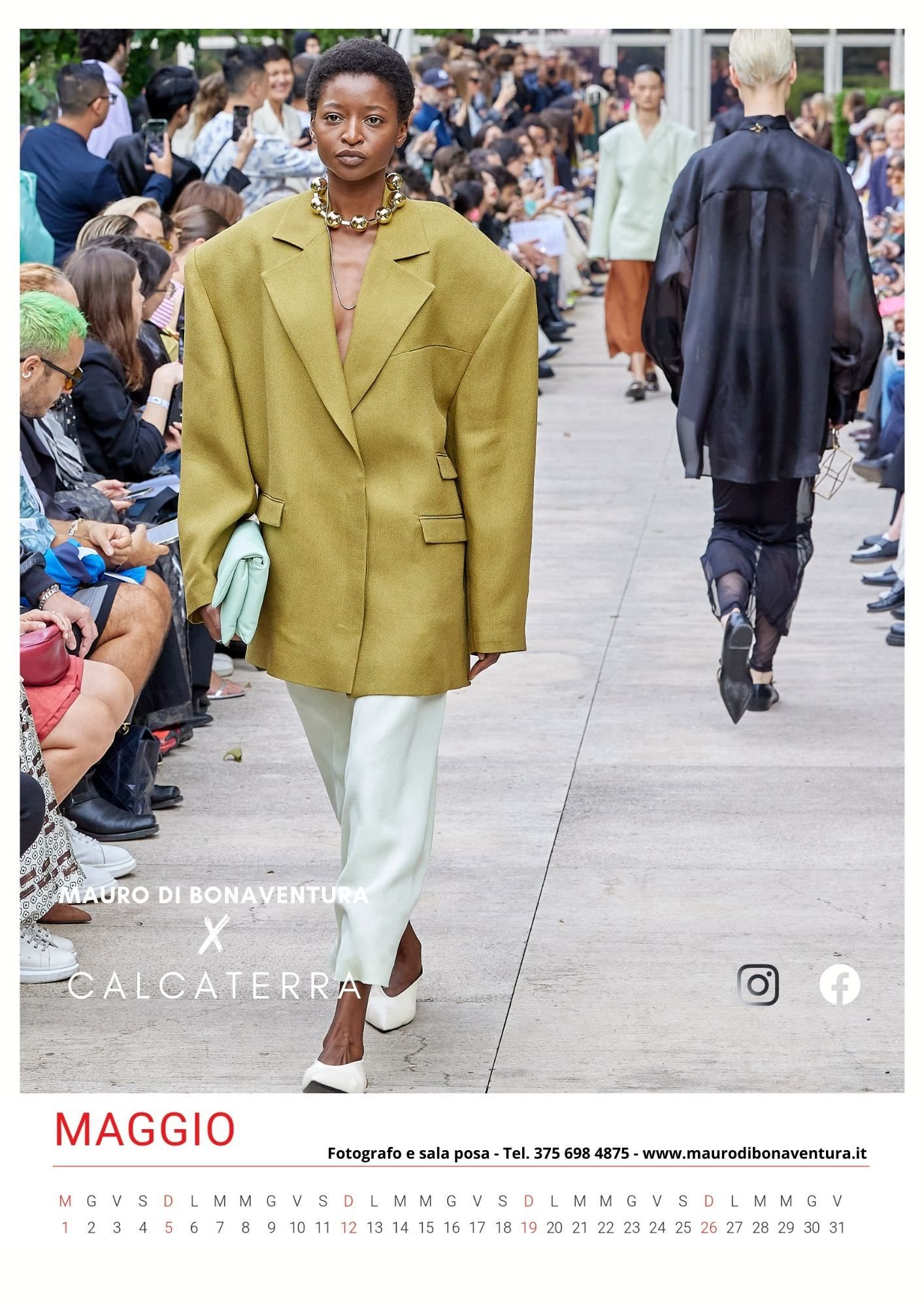 Oversized mustard yellow blazer paired with white pants shown on outdoor runway.