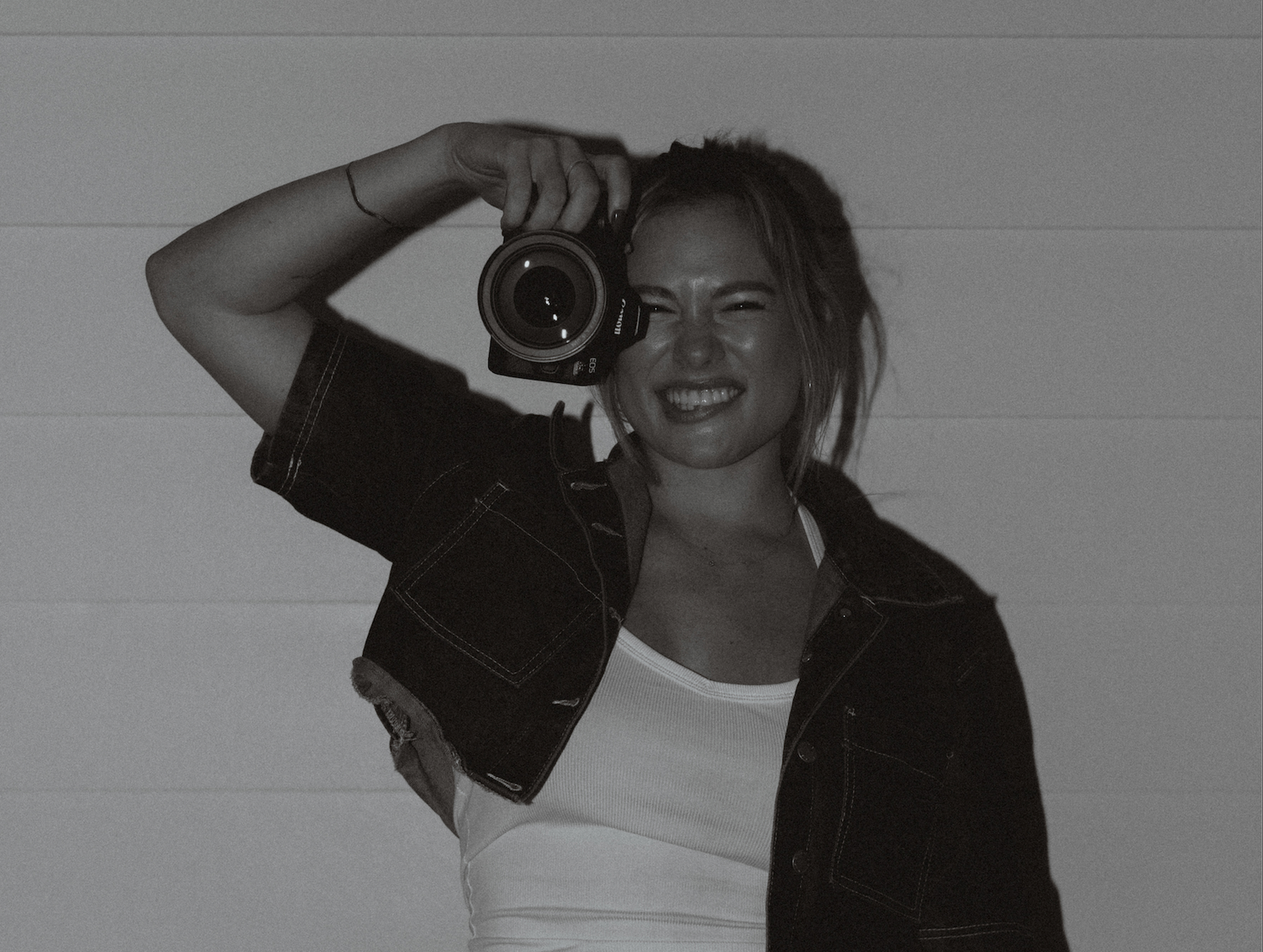 Young woman smiling while holding a camera up to her eye in a black and white photo.
