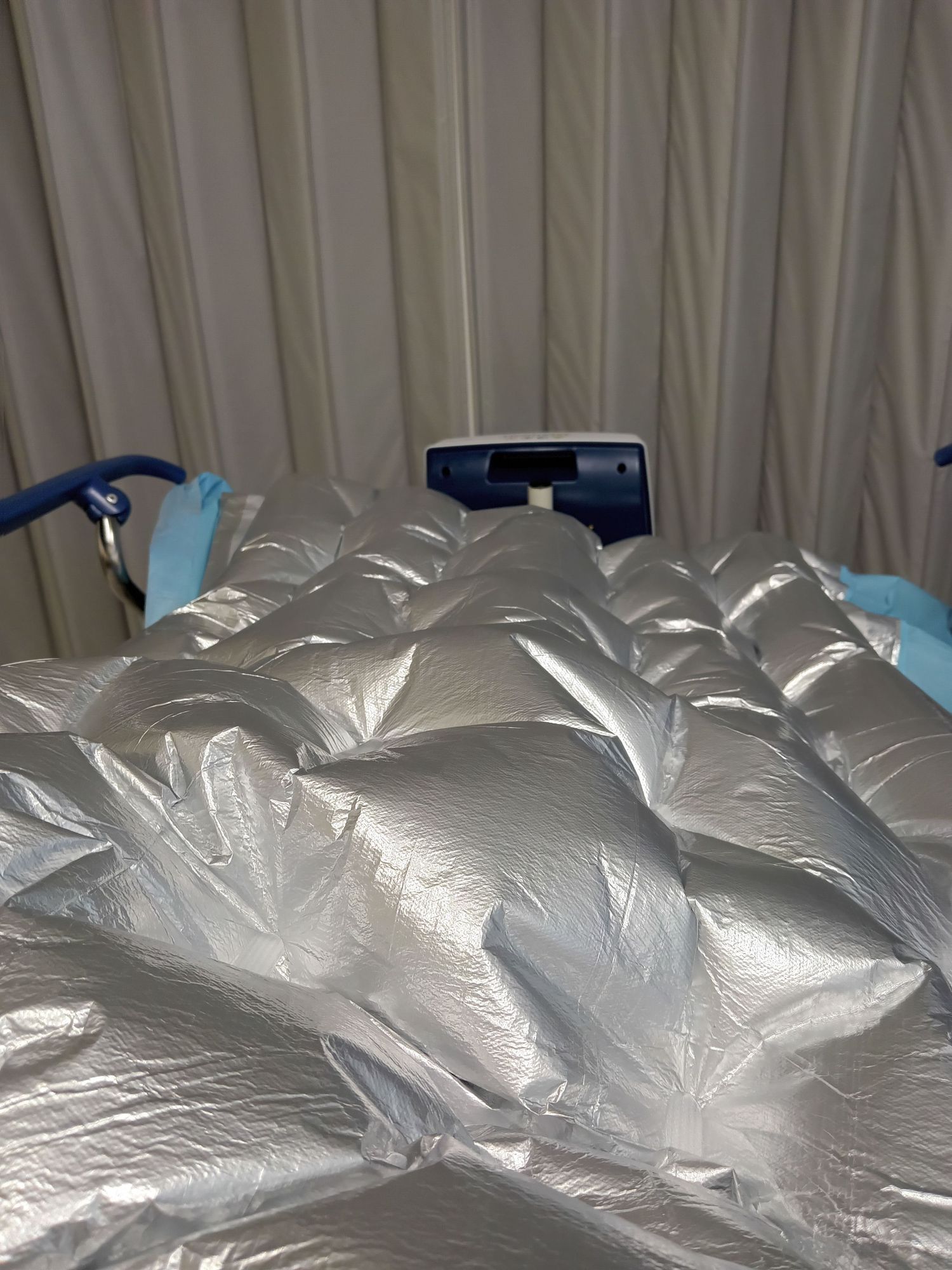 Medical supplies or packages covered in silver sterile wrapping on a hospital bed.