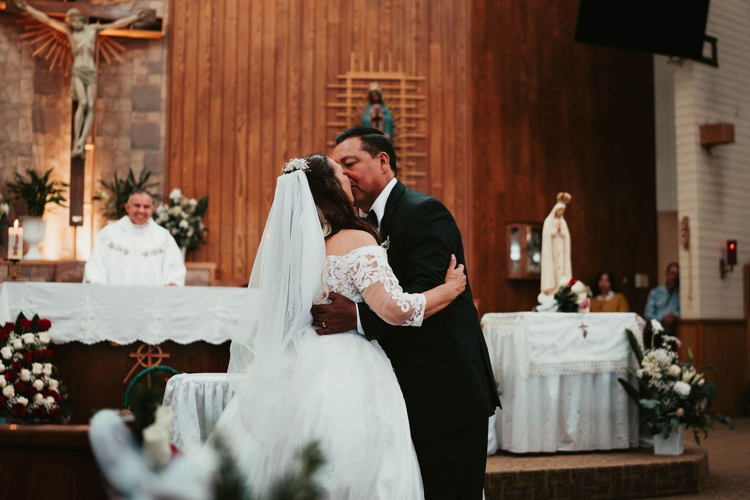 A romantic wedding ceremony kiss in a church with wooden interior and altar decorations.