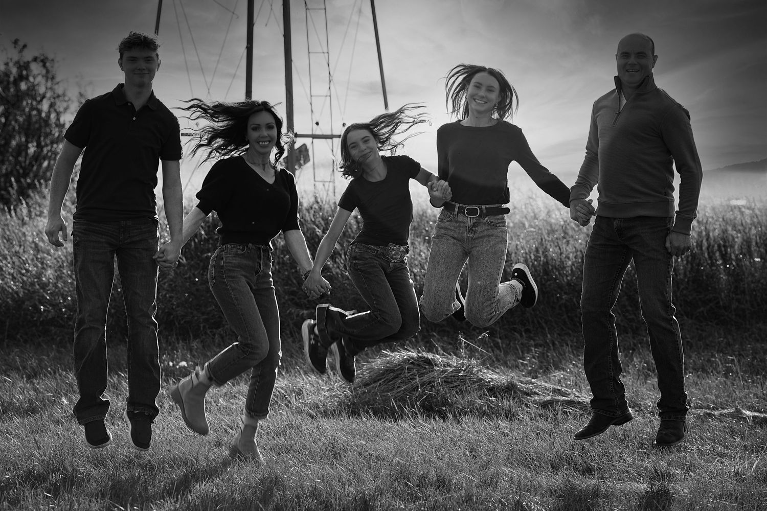 A black and white photo of five people jumping joyfully in unison on a grassy hillside silhouetted against the sky.